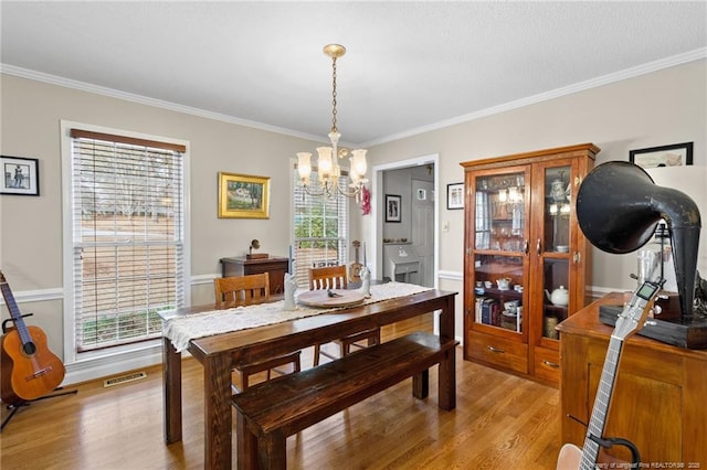 dining space with visible vents, light wood-style flooring, an inviting chandelier, and ornamental molding