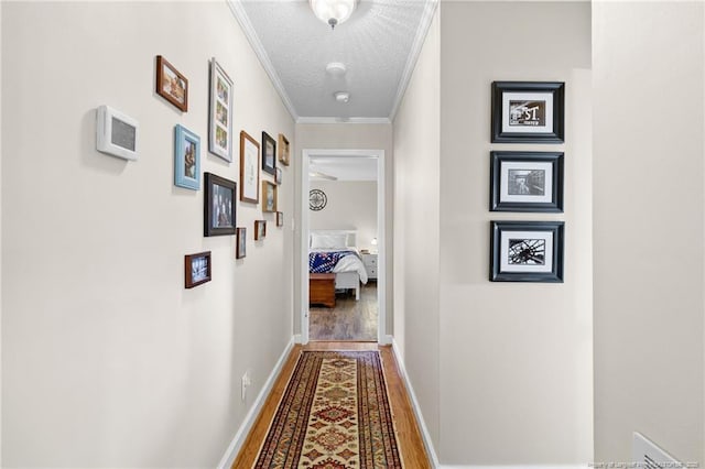 corridor with baseboards, a textured ceiling, wood finished floors, and crown molding