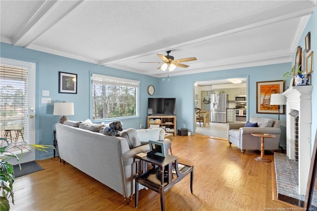 living area featuring beam ceiling, a brick fireplace, wood finished floors, and ceiling fan