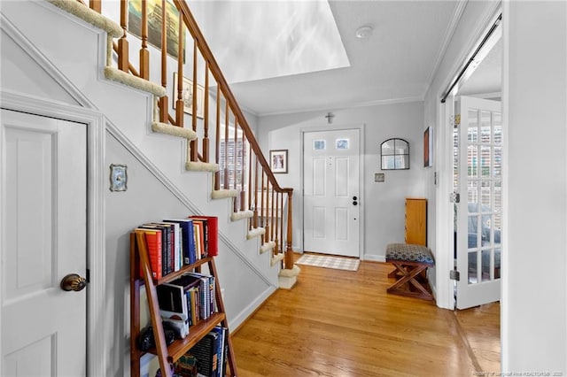 foyer featuring stairs, baseboards, light wood-type flooring, and ornamental molding