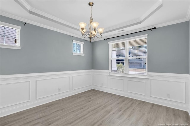 unfurnished room with a raised ceiling, a notable chandelier, wood finished floors, and visible vents