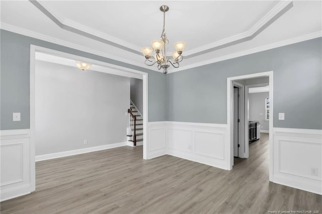 empty room featuring wood finished floors, a raised ceiling, a chandelier, and stairs