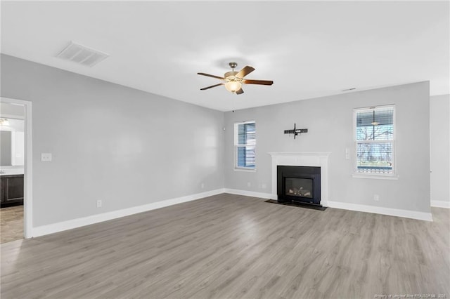 unfurnished living room with light wood-type flooring, visible vents, a fireplace with flush hearth, a ceiling fan, and baseboards