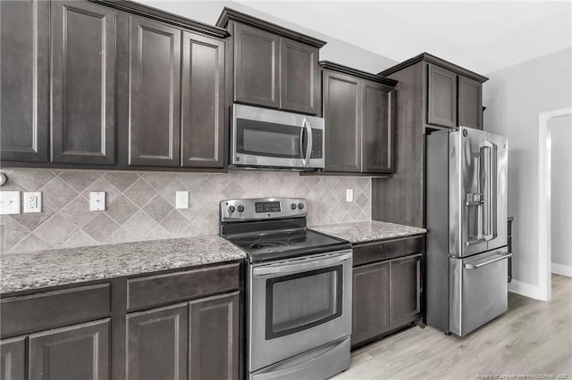 kitchen with dark brown cabinets, light stone counters, decorative backsplash, appliances with stainless steel finishes, and light wood-style floors