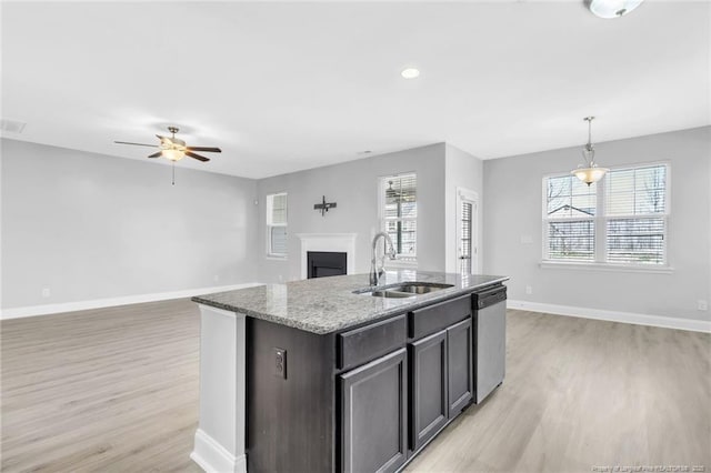 kitchen featuring baseboards, a fireplace, a sink, stainless steel dishwasher, and open floor plan