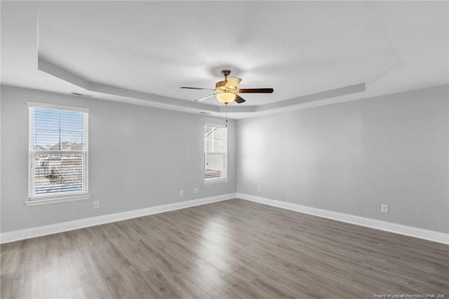 empty room with ceiling fan, baseboards, a raised ceiling, and wood finished floors