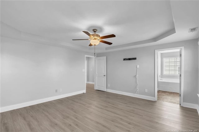 spare room with a ceiling fan, visible vents, baseboards, light wood-style flooring, and a raised ceiling