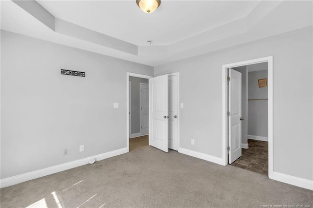 unfurnished bedroom with carpet flooring, a raised ceiling, and baseboards