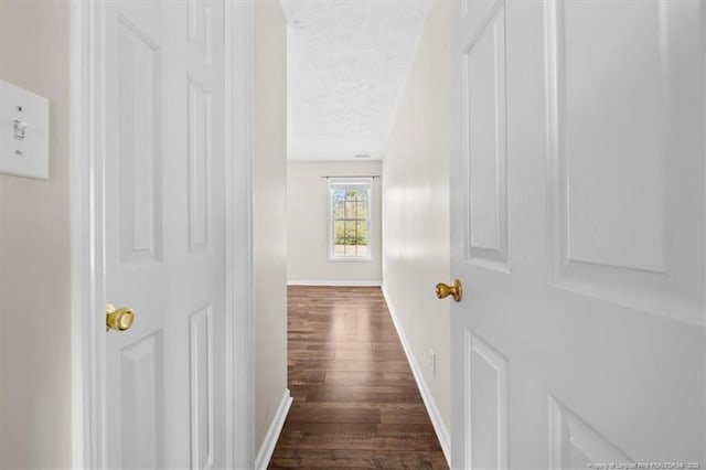 hallway with dark wood finished floors, a textured ceiling, and baseboards