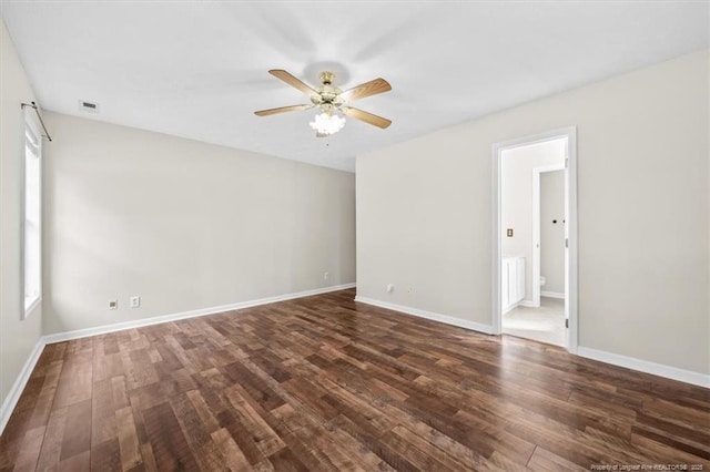 spare room with dark wood finished floors, baseboards, visible vents, and ceiling fan