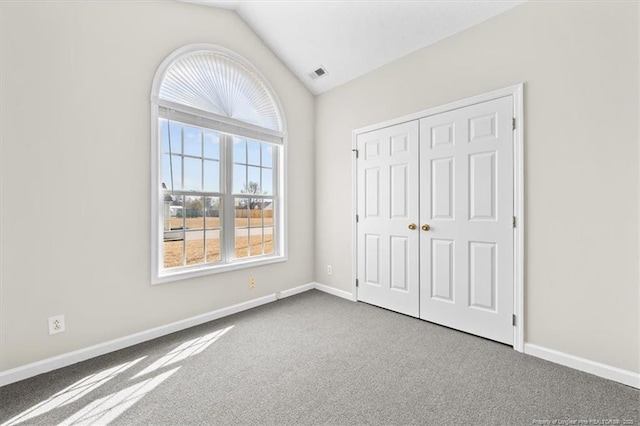 unfurnished bedroom featuring carpet, visible vents, baseboards, lofted ceiling, and a closet