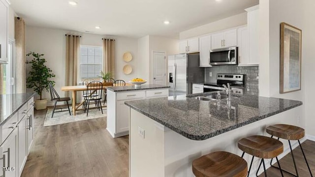 kitchen with wood finished floors, white cabinetry, appliances with stainless steel finishes, a peninsula, and decorative backsplash