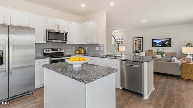 kitchen featuring open floor plan, dark stone counters, appliances with stainless steel finishes, a peninsula, and a sink