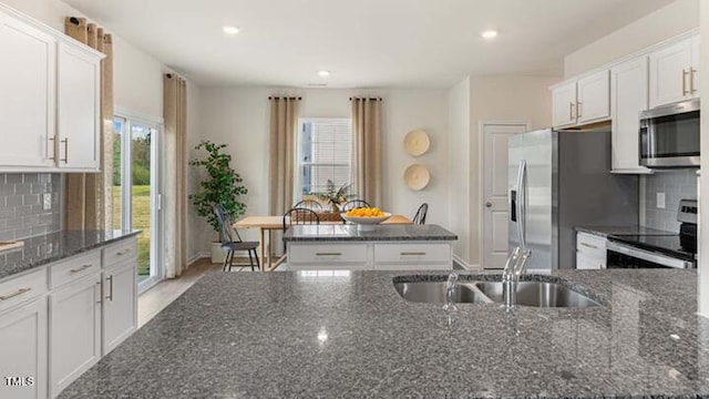 kitchen with dark stone countertops, white cabinetry, stainless steel appliances, and a sink