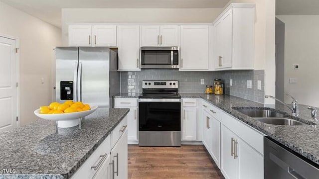 kitchen with white cabinets, appliances with stainless steel finishes, dark stone counters, and a sink