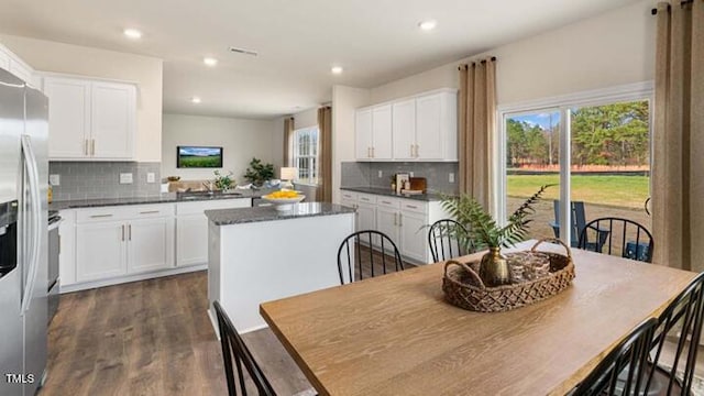 kitchen with dark countertops, stainless steel refrigerator with ice dispenser, white cabinets, and a center island