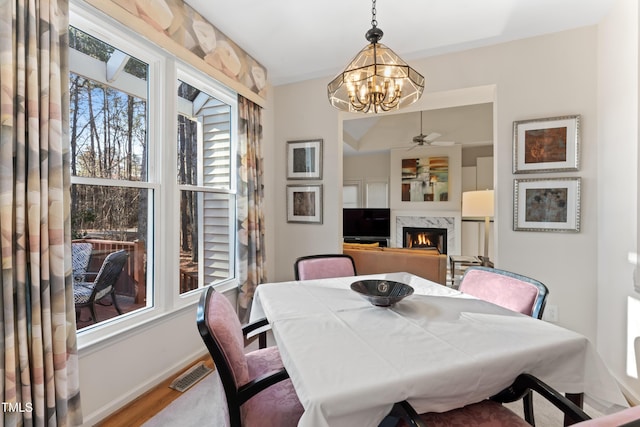 dining area featuring visible vents, baseboards, ceiling fan with notable chandelier, a fireplace, and wood finished floors