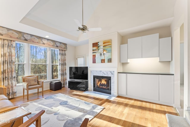 unfurnished living room with light wood-type flooring, a tray ceiling, a fireplace, and a ceiling fan