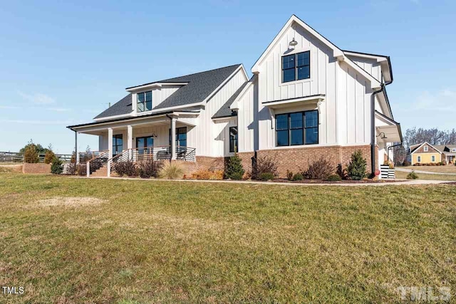 modern farmhouse style home featuring a front lawn, covered porch, brick siding, and board and batten siding