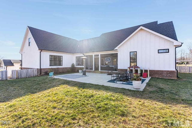 rear view of property featuring brick siding, a patio area, a lawn, and fence