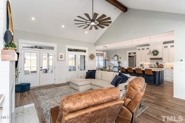 living area with wood finished floors, french doors, beam ceiling, and a wainscoted wall