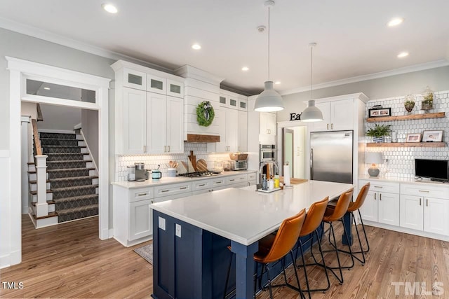 kitchen with light wood-style flooring, ornamental molding, light countertops, appliances with stainless steel finishes, and white cabinetry