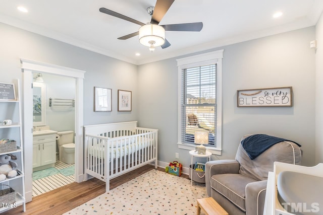 bedroom featuring a crib, baseboards, light wood-style floors, and ornamental molding