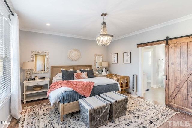 bedroom featuring ornamental molding, a barn door, and wood finished floors