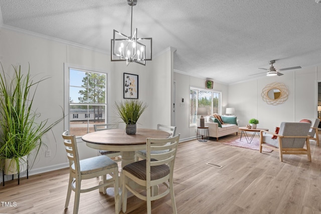 dining space with light wood finished floors, ceiling fan with notable chandelier, a textured ceiling, and ornamental molding