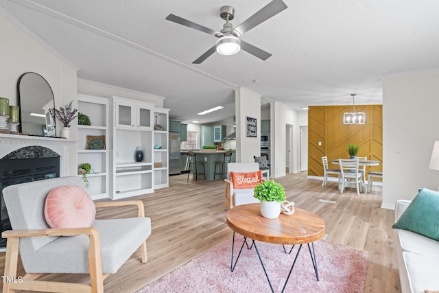 living area featuring a high end fireplace, light wood-style flooring, ceiling fan with notable chandelier, and ornamental molding