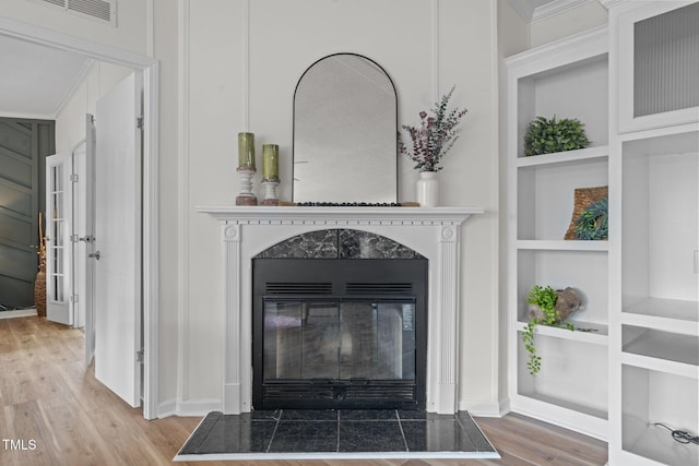 room details with a premium fireplace, visible vents, built in shelves, and wood finished floors