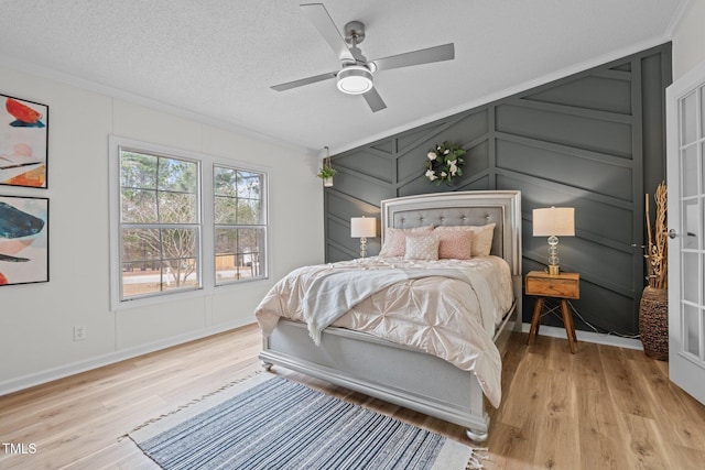 bedroom featuring a decorative wall, ornamental molding, light wood-type flooring, and a textured ceiling