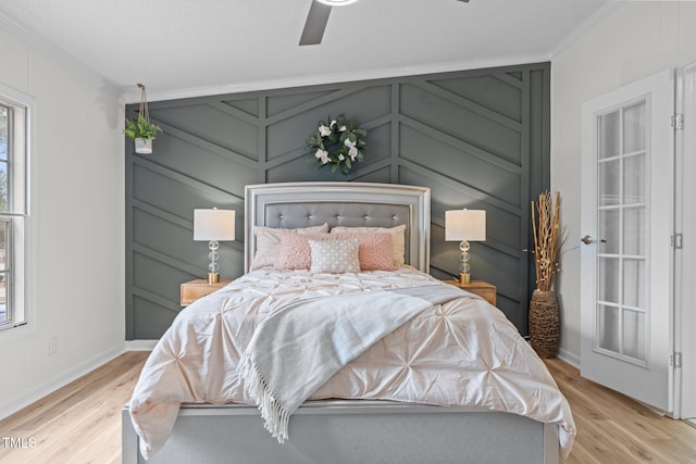 bedroom featuring baseboards, ceiling fan, crown molding, a decorative wall, and light wood-type flooring