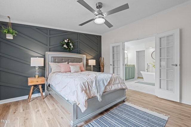 bedroom featuring light wood finished floors, ornamental molding, french doors, ensuite bathroom, and a decorative wall