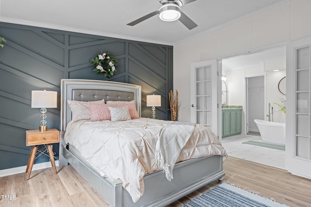 bedroom featuring connected bathroom, crown molding, ceiling fan, light wood-type flooring, and a decorative wall