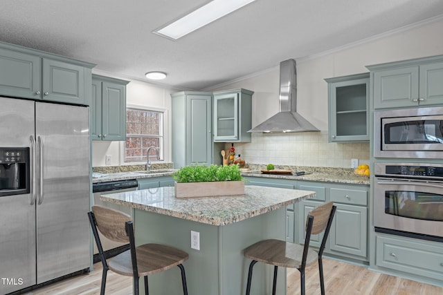 kitchen featuring wall chimney range hood, a kitchen bar, light wood-style flooring, appliances with stainless steel finishes, and a sink