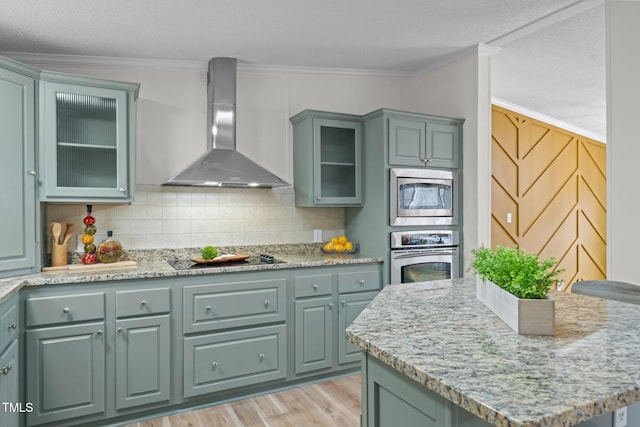 kitchen with decorative backsplash, appliances with stainless steel finishes, wall chimney exhaust hood, and ornamental molding