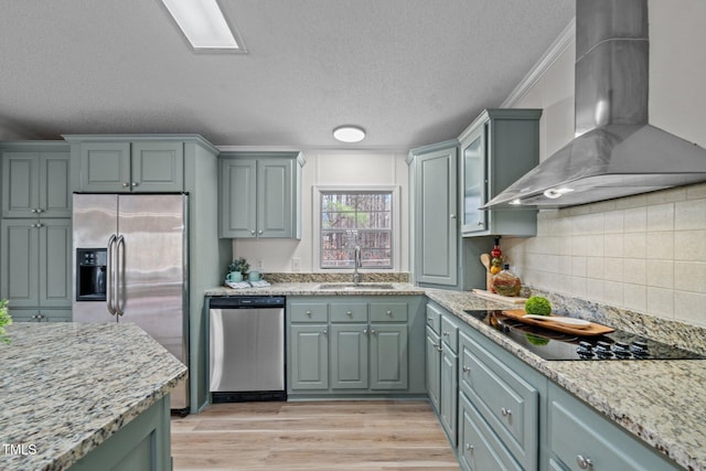 kitchen with a sink, wall chimney range hood, backsplash, stainless steel appliances, and light wood finished floors