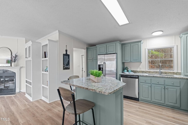 kitchen featuring light wood-type flooring, a sink, a kitchen island, stainless steel appliances, and a breakfast bar area