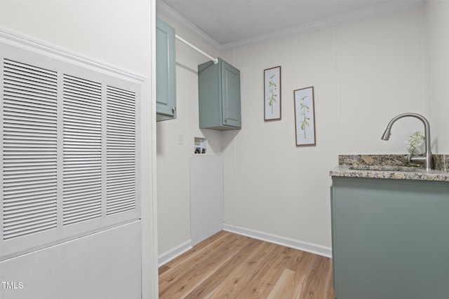 clothes washing area featuring light wood-style flooring, ornamental molding, a sink, baseboards, and a heating unit