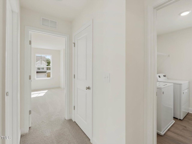 corridor featuring separate washer and dryer, light colored carpet, visible vents, and baseboards