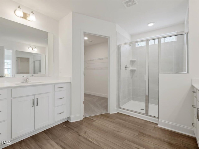 full bathroom with a spacious closet, visible vents, a stall shower, wood finished floors, and vanity