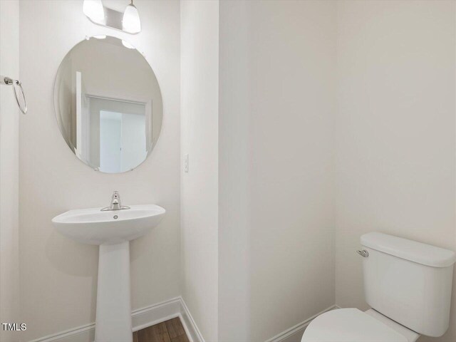 half bath with toilet, baseboards, and wood finished floors