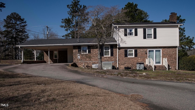 split level home featuring an attached carport, entry steps, central AC unit, a chimney, and driveway