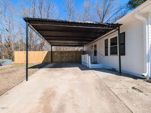 view of parking / parking lot featuring an attached carport, concrete driveway, and fence