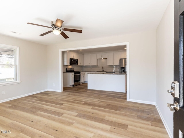 kitchen featuring backsplash, baseboards, light wood-style flooring, stainless steel appliances, and a ceiling fan