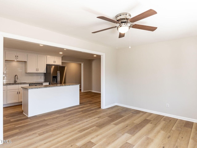 kitchen with a ceiling fan, stainless steel fridge with ice dispenser, a sink, light wood-style floors, and tasteful backsplash