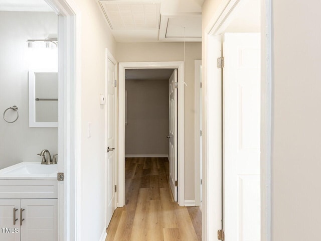 hall featuring light wood finished floors, visible vents, baseboards, attic access, and a sink