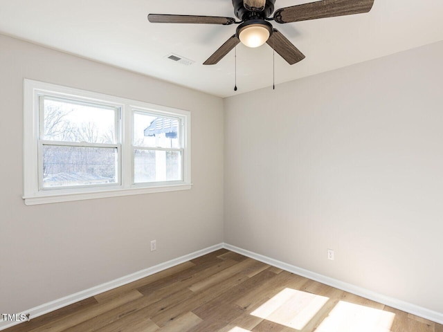 spare room with ceiling fan, visible vents, baseboards, and wood finished floors