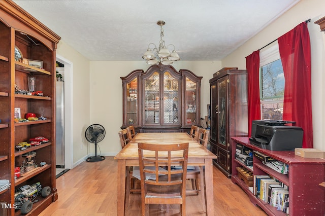 dining room featuring a chandelier, light wood-style flooring, a textured ceiling, and baseboards